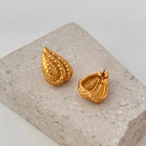 Macro-opname van gouden druppeloorbellen met gehamerde textuur op een steenbasis