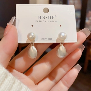 Detalle de pendientes de perlas blancas con colgantes de gota plateada mate y aguja de S925