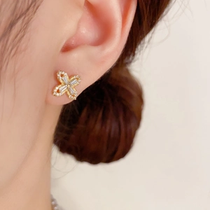 Close-up of sparkling gold four-leaf clover stud earrings with pavé-set zircons on ear