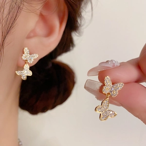 Close-up of gold double butterfly drop earrings encrusted with sparkling white zircons