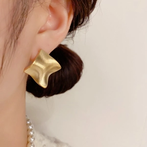 Close-up of matte gold geometric rhombus earrings worn with a white pearl necklace