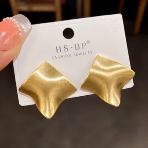 Vue macro de boucles d'oreilles losanges en métal brossé doré avec surface texturée