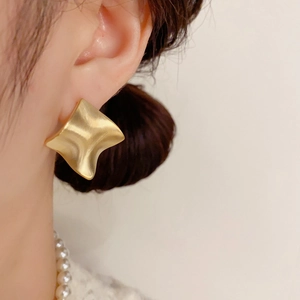 Close-up of matte gold geometric rhombus earrings with brushed texture on model