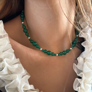 Detail of green agate beaded necklace with gold spacers worn by model on white background