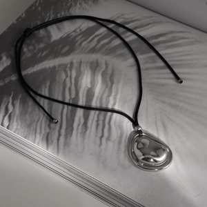 Irregular silver pendant necklace with black cord on minimalist aesthetic background