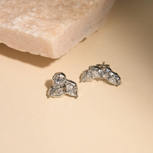 Elegant silver-toned 18K gold plated zircon stud earrings on a beige stone background