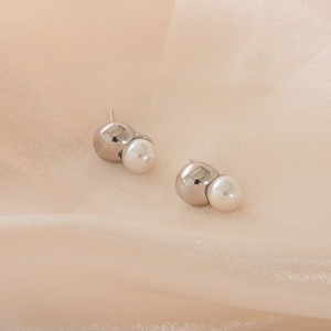 Macro detail of minimalist silver metal and pearl stud earring on champagne silk