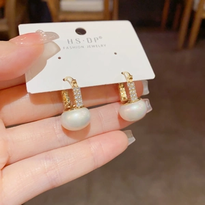 Macro detail of gold U-shaped earrings featuring square diamonds and glossy pearls