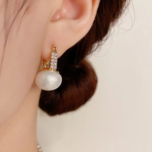 Close-up of geometric gold huggie hoop earring with pave zircons and white round pearl