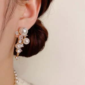 Détail de boucles d'oreilles dorées avec perles blanches et pompons en zircone cubique