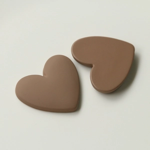 Macro detail of two matte coffee brown heart-shaped acrylic hair clips on beige surface