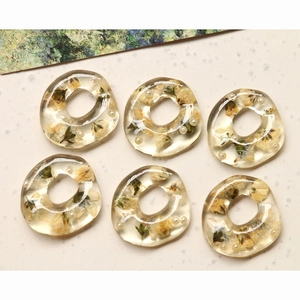 Detailed view of six handmade resin rings with yellow dried flowers and white pearls