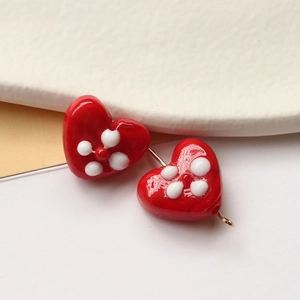 Macro shot of red heart-shaped glass beads with white flower patterns and gold hooks