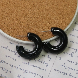 Close-up of black resin C-shaped hoop earrings with silver pins on cork and paper background