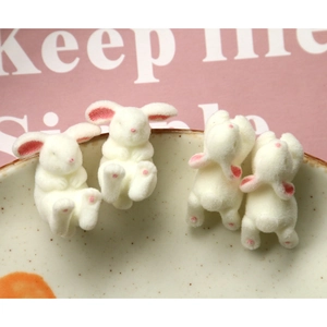 Detail showing four white flocked rabbit charms in sitting and crawling poses for DIY