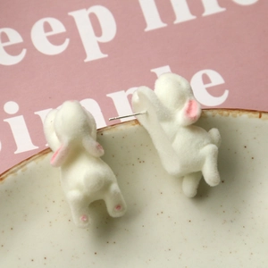 Detail of cute white flocked bunny earrings with pink accents on a ceramic plate