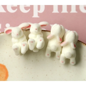Detailed macro view of four cute flocked white rabbit resin charms with soft pink accents