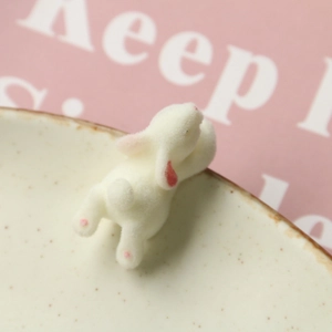 Close-up of a white flocked bunny resin charm peeking over a ceramic bowl edge