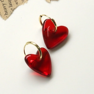 Détail de boucles d'oreilles créoles dorées avec coeurs en résine rouge translucide