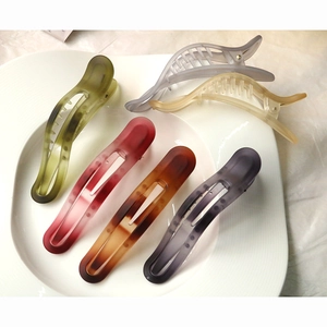 Close-up of five colorful matte resin duckbill hair clips on a white ceramic plate