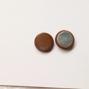 Detailed view of round brown leather magnetic buttons showing front and back textures