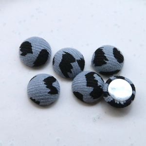 Close-up of six fabric-covered decorative buttons with grey black abstract patterns