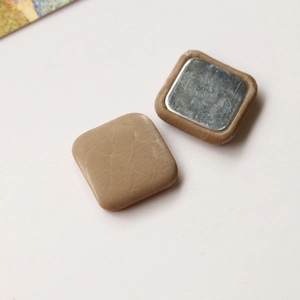 Detail of square khaki snakeskin velvet button showing leather texture and metal backing
