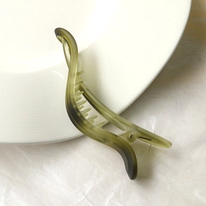 Macro view of olive green matte hair clip with curved design on white ceramic plate