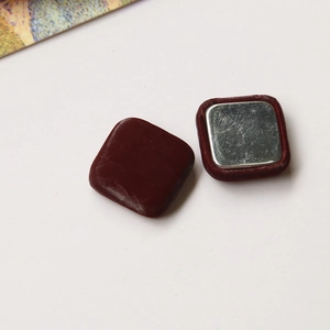 Detail view of square magnetic buttons with deep wine red leather texture and metal back