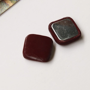 Detailed close-up of burgundy leather magnetic buckles for coat and bag DIY decoration