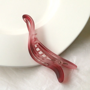 Close-up of matte dark red resin hair clip with twisted design on white plate