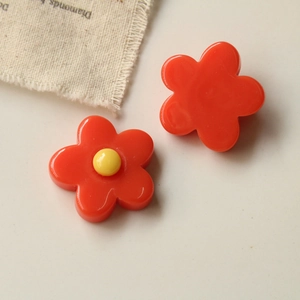 Detailed macro view of red resin flower accessories with yellow center on white linen fabric