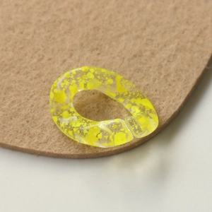 Detail view of a clear acrylic ring with vibrant yellow ink splatter effect for DIY jewelry