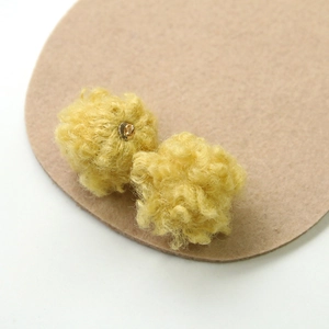 Detailed texture of bright yellow faux lamb wool ball with a gold hanging loop connector