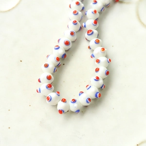 Macro view of handmade white glass evil eye beads with red and blue dots on a metal chain