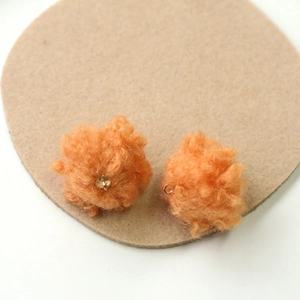 Detailed view of orange plush pom-pom charms with gold metal loops for DIY jewelry making