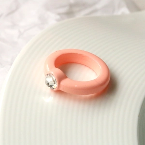 Anello in acrilico arancio rosa con strass rotondo su un piatto di ceramica bianca