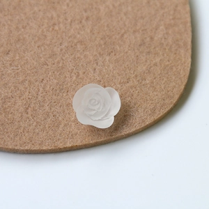Close-up of a matte white resin rose charm for DIY jewelry on a brown felt base