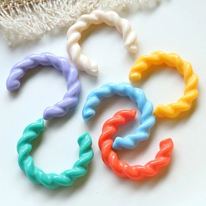 Accessori in acrilico intrecciati a forma di C in tonalità pastello su fondo bianco