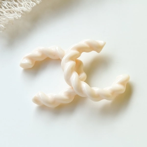 Dettaglio di orecchini a forma di C intrecciati color crema con finitura in resina lucida