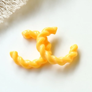 Dettaglio ravvicinato di componenti artigianali in acrilico giallo a forma di C intrecciata