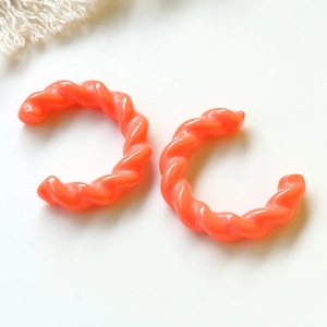 Dettaglio di orecchini a cerchio a C in resina arancione con design a spirale lucida