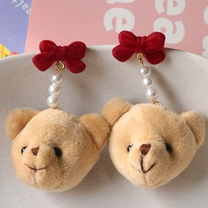Détail de boucles d'oreilles ours en peluche avec nœuds en velours rouge et perles blanches