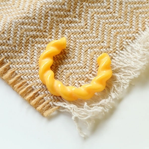 Accessorio anello a C intrecciato in resina giallo lucido su un tappeto intrecciato