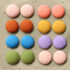 Dettaglio macro di sedici bottoni colorati rivestiti in tessuto su sfondo grigio opaco