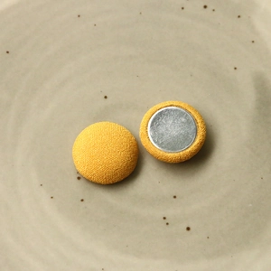 Dettaglio dei bottoni rotondi ricoperti in tessuto giallo con retro in metallo argento
