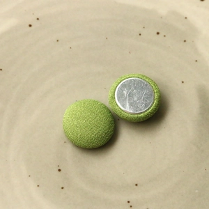 Dettaglio di bottoni tondi in tessuto verde erba con base posteriore in metallo argento
