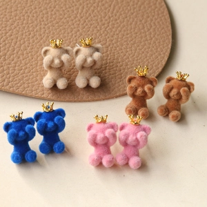 Macro detail of plush crown bear earrings in beige, brown, blue, and pink flocking