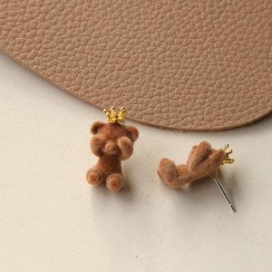 Macro shot of brown flocked teddy bear earrings with tiny gold crowns and silver needles