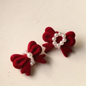 Macro detail of red velvet bow earrings featuring elegant white pearl center accents